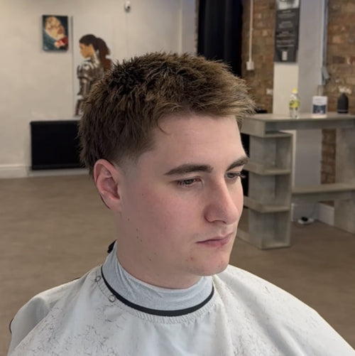 Man getting a haircut in a barbershop with a white cape on